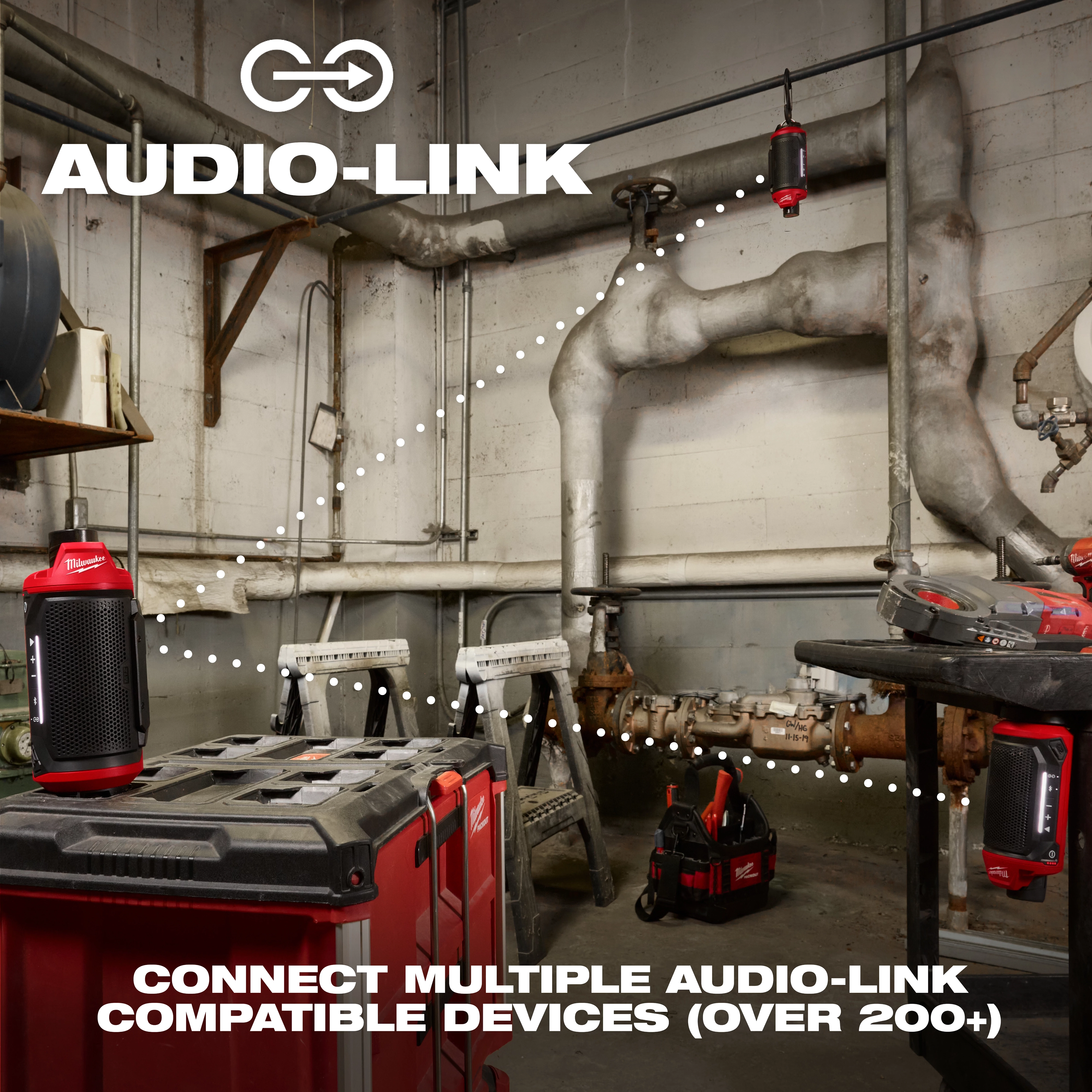 A workshop with an M12™ Bluetooth® Jobsite Speaker w/ PACKOUT™ Compatibility is displayed. The image highlights the connectivity feature "Audio-Link" with multiple speakers linked through dotted lines. The text reads, "CONNECT MULTIPLE AUDIO-LINK COMPATIBLE DEVICES (OVER 200+)." Various tools are also visible in the background.