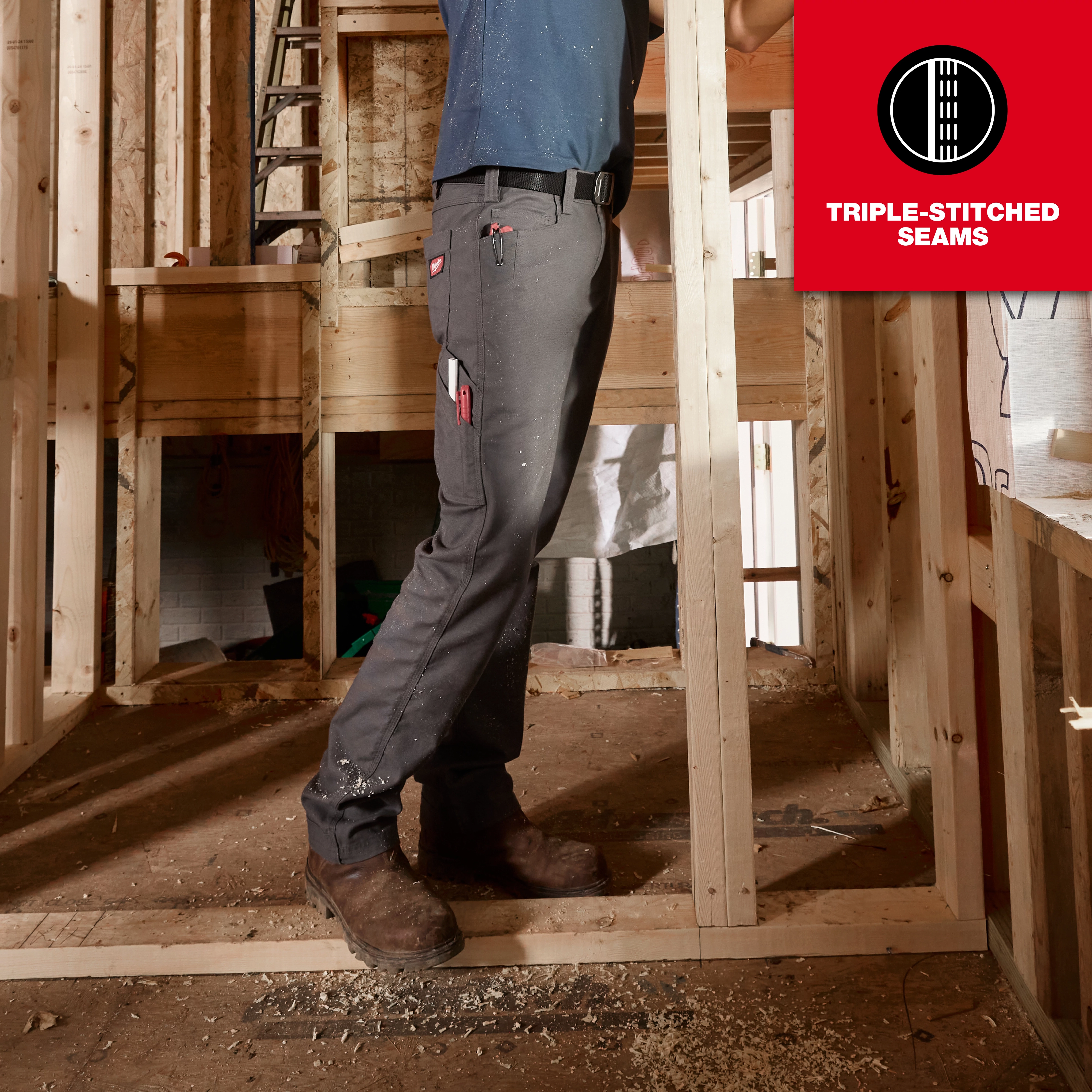 A man wearing Work Pants stands at a construction site. The pants are gray with several pockets, a tool hanging from one, and feature triple-stitched seams. The image emphasizes the durability and functionality of the Work Pants.