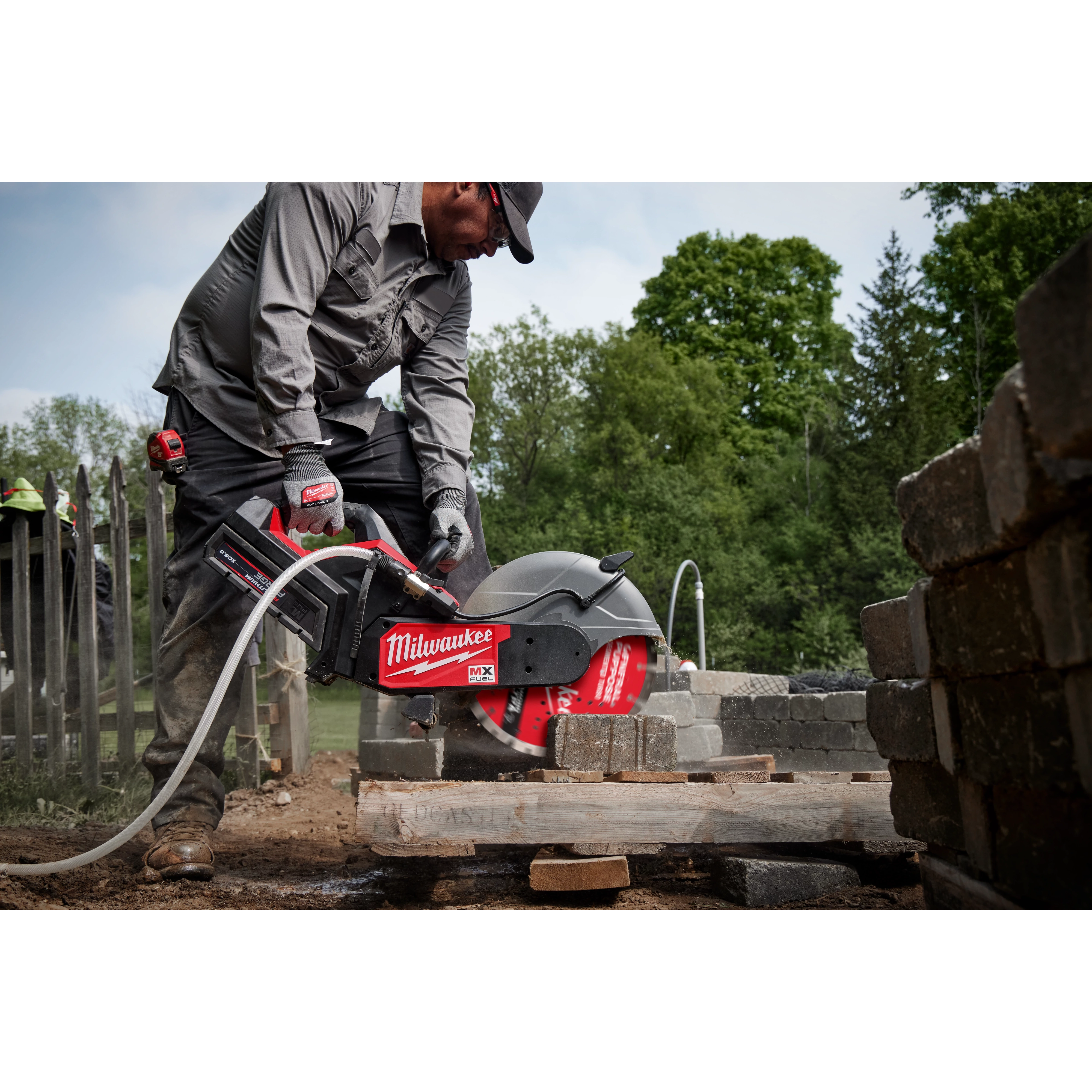 A person is using a Milwaukee saw fitted with a 14-inch DIAMOND ULTRA™ Segmented Turbo, General Purpose Diamond Blade to cut concrete blocks outdoors. The saw and blade are part of Milwaukee's MX FUEL equipment, visible against a background of trees and construction materials.