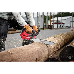 Person using a red Milwaukee chainsaw to cut a large log outdoors, wearing protective gloves and jacket.