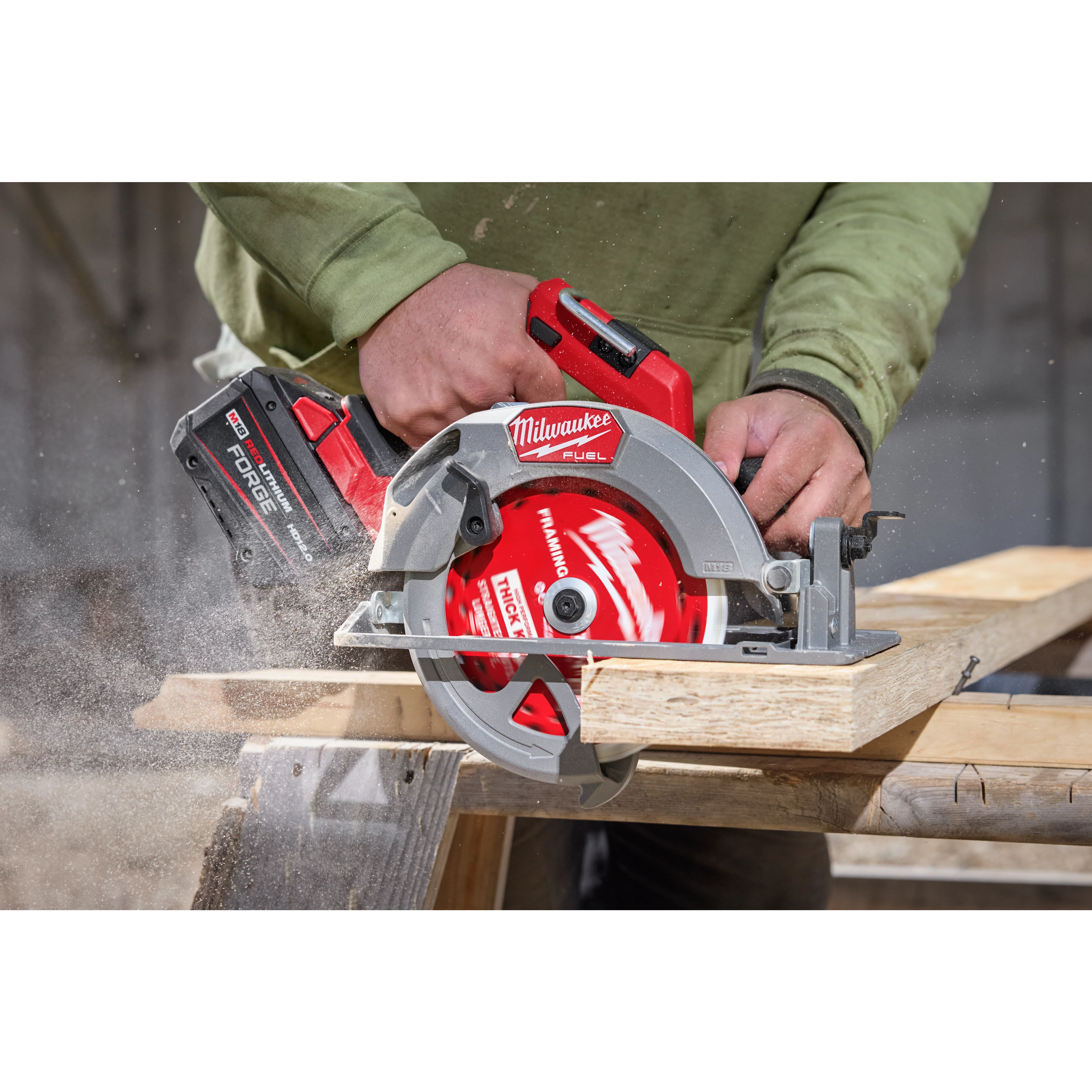 A person is using a red Milwaukee circular saw with a 7-1/4" 24T Thick Kerf Framing Circular Saw Blade to cut wood. Sawdust is visible from the cutting action. The circular saw has a black and red battery pack attached.